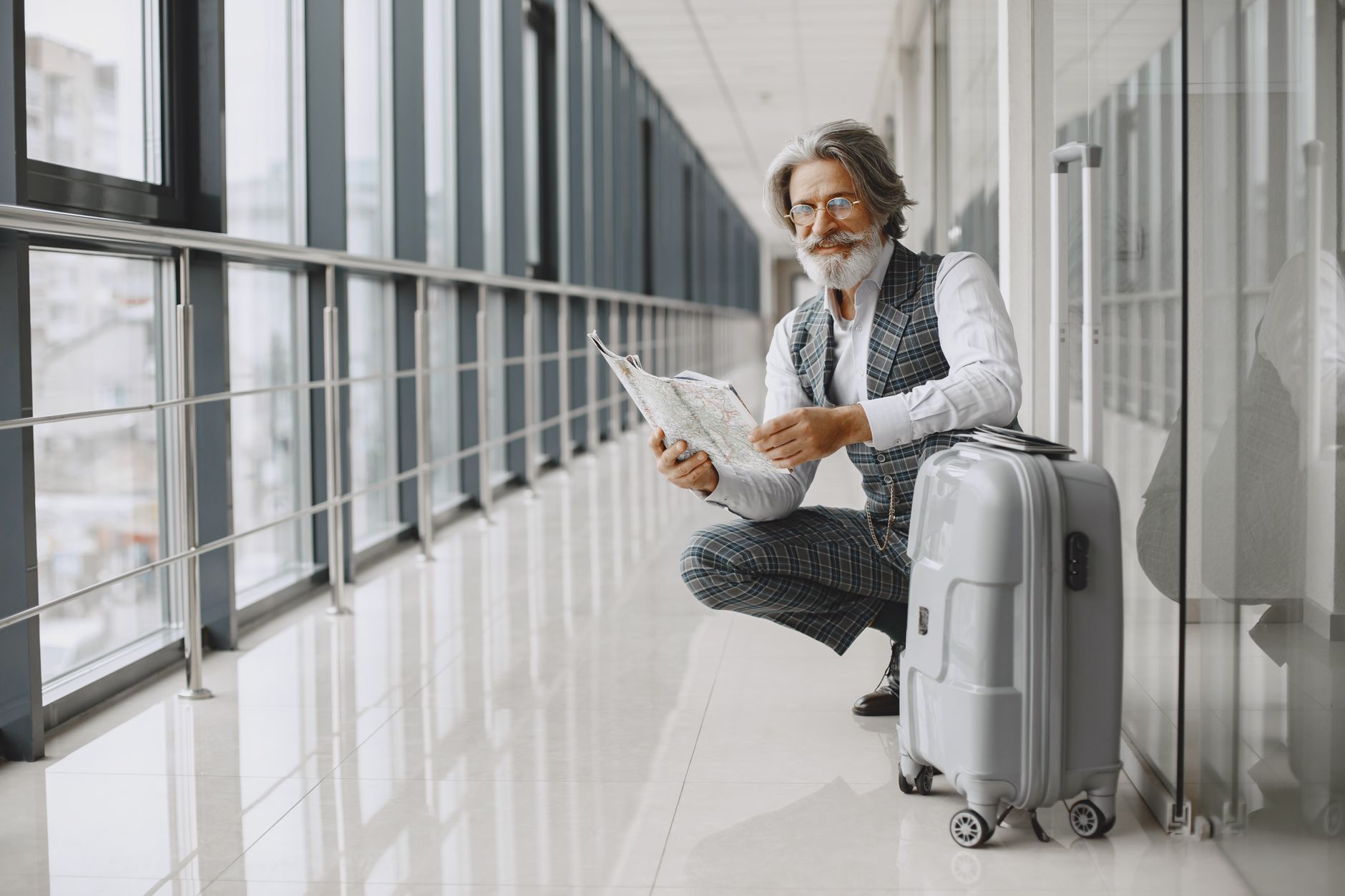 Senior man in airport hallway holding a map, sitting beside luggage, illustrating travel and exploration.